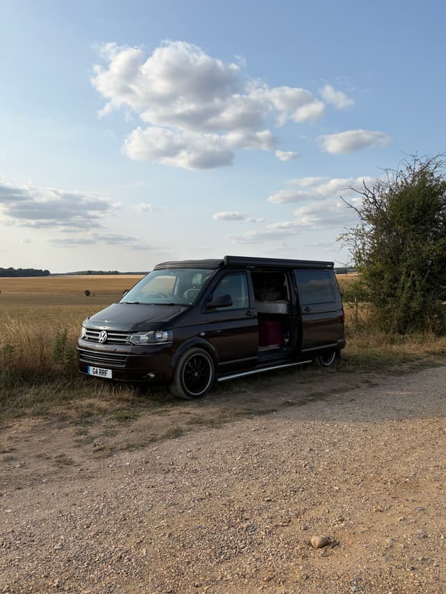 Black Volkswagen camper van parked by fields